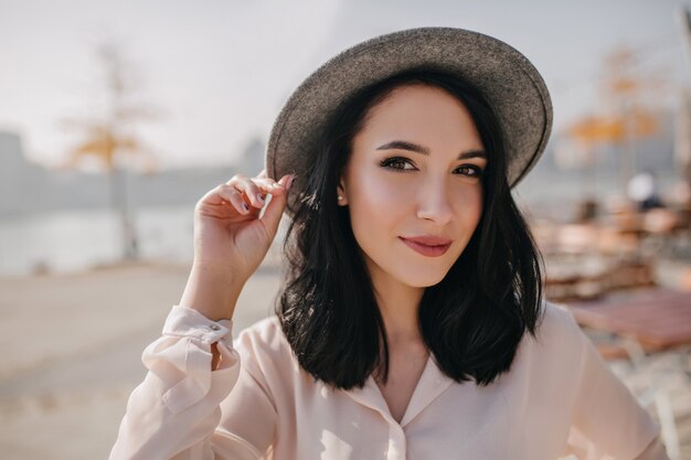 Joyful dark-eyed woman playfully posing on blur nature wall in morning