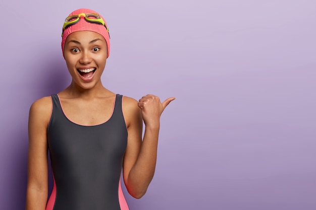 Free photo joyful dark skinned female swimmer wears bathingcap, black swimsuit