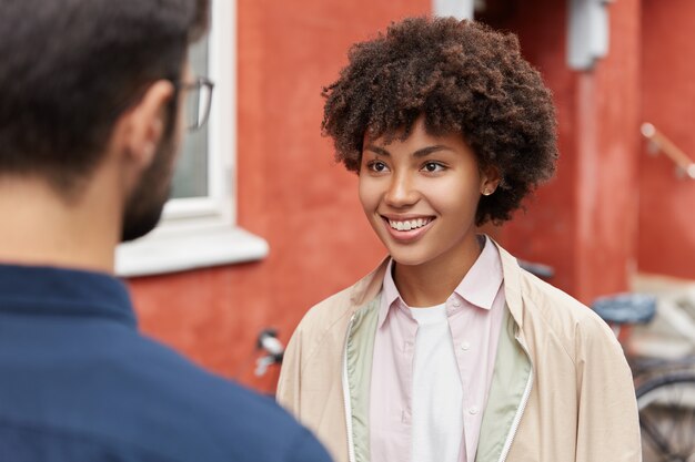Joyful dark skinned woman with toothy smile, wears casual coat