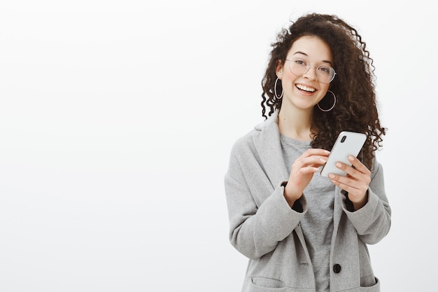 Joyful emotive young european woman in glasses and grey coat with stylish round earrings