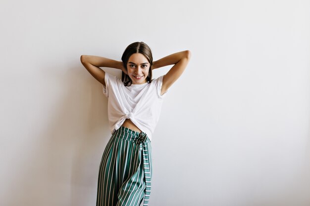 Joyful female model in pajama playing with her hair. Laughing young woman in green pants standing