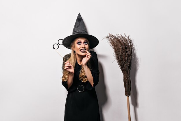 Joyful female model with dark makeup preparing for carnival. Jocund girl in halloween costume making funny faces.