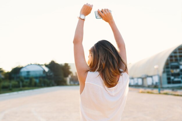 Joyful girl dancing in the street on a sunny day holding hands up