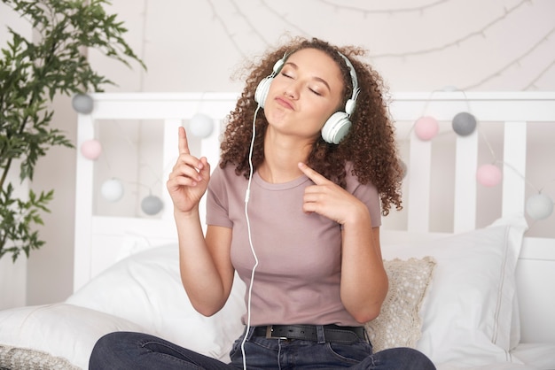 Бесплатное фото Радостная девушка слушает музыку и танцует на кровати