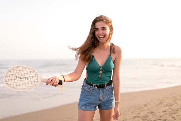 Joyful girl playing tennis with racket at beach