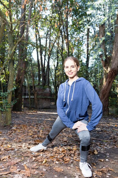 Joyful girl with sweatshirt stretching her legs in the park