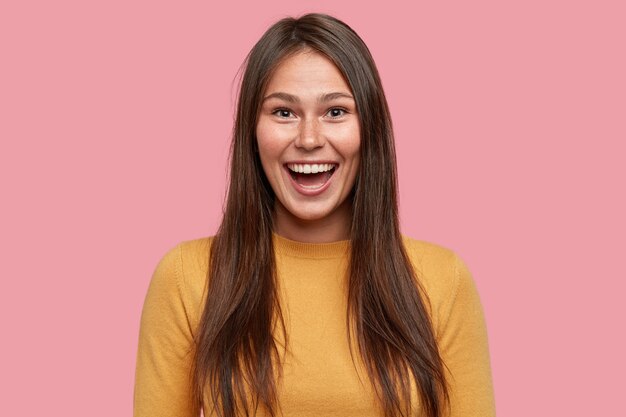 Joyful good looking brunette girl, smiles from happiness, feels joyful and amused