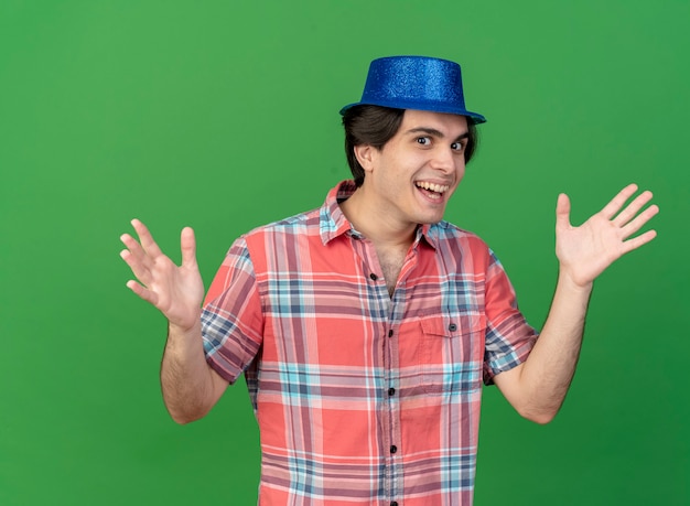 Joyful handsome caucasian man wearing blue party hat holds hands open 