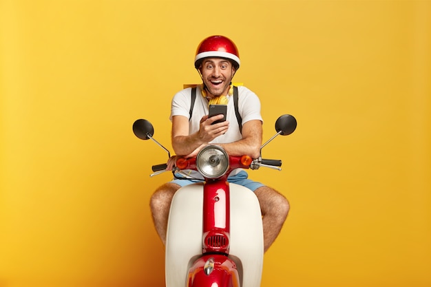 Joyful handsome male driver on scooter with red helmet