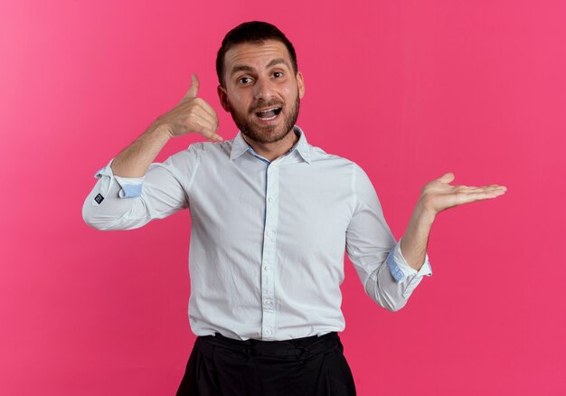 Joyful handsome man gestures call me hand sign holds empty hand open isolated on pink wall