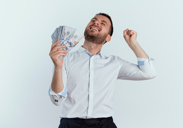 Joyful handsome man holds money and raises fist isolated on white wall