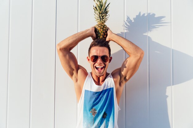 Joyful handsome man in sunglasses holds a pineapple on his head