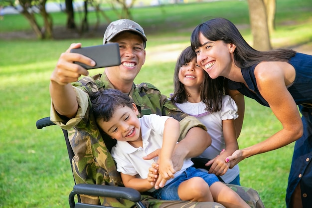無料写真 公園で彼の妻と2人の子供と一緒に自分撮りをしているうれしそうな幸せな障害者の軍人。家族の一体感とサポートの概念