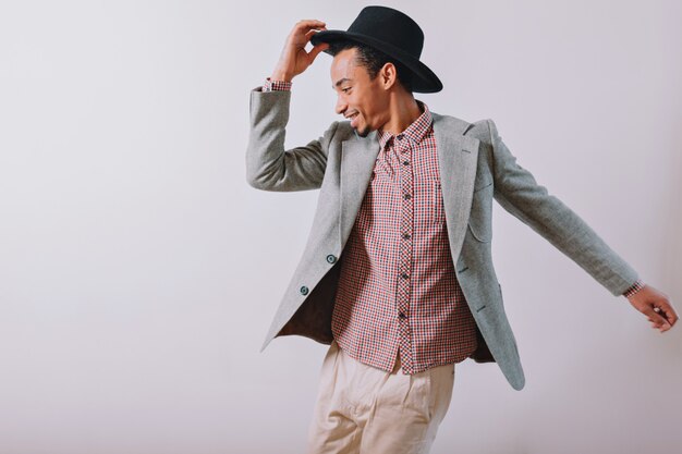 Joyful happy man wears black hat and grey suit dancing with excited emotions on gray