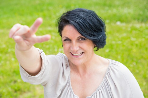 Joyful happy middle aged woman showing peace sign