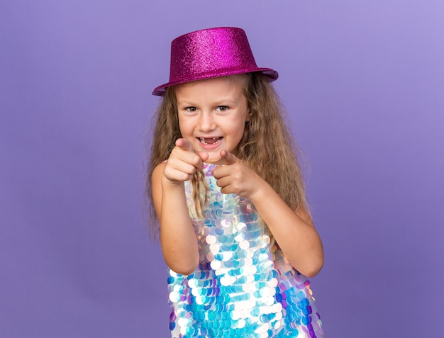 радостная маленькая блондинка с фиолетовой шляпой, указывая на фиолетовую стену с копией пространства