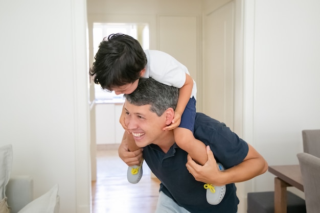 Ragazzino allegro che si siede sulle spalle del padre e che ride.