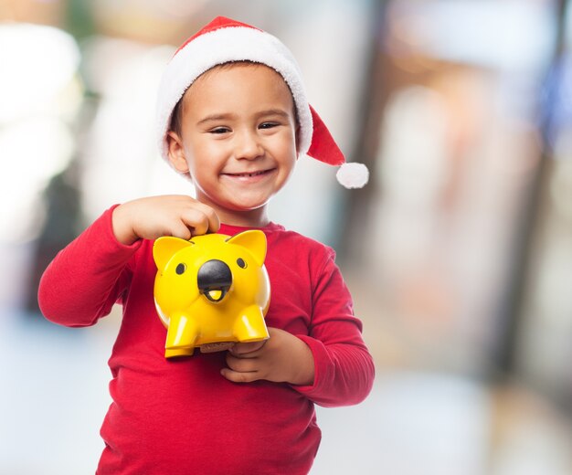 Joyful little boy with piggybank and santa claus hat