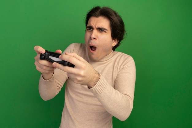 Gioioso guardando al lato giovane bel ragazzo tenendo il controller di gioco joystick isolato sulla parete verde