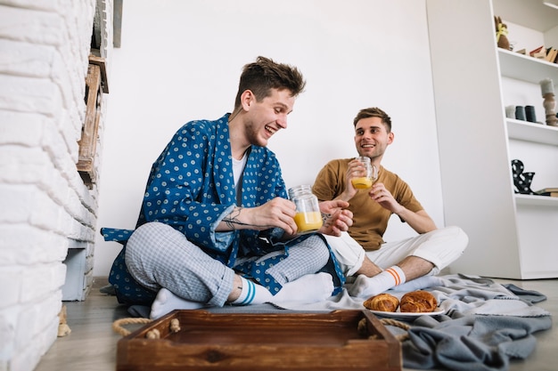 Joyful male friends enjoying tasty breakfast sitting on floor at home