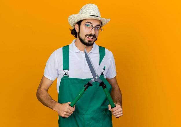 Joyful male gardener in optical glasses wearing gardening hat holds clippers