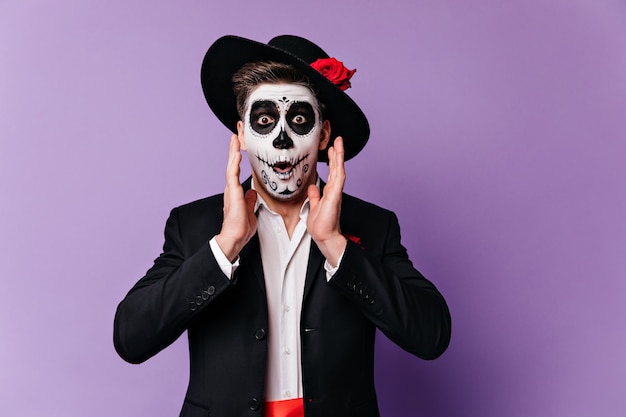 Joyful man with halloween makeup in shock looks into camera, posing on purple background