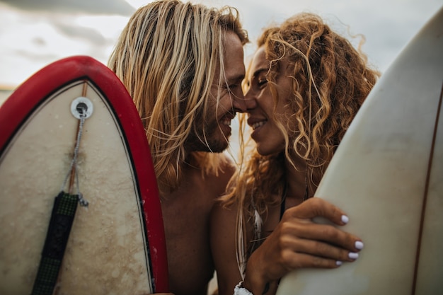 Foto gratuita bacio gioioso di uomo e donna. coppie che tengono le tavole da surf