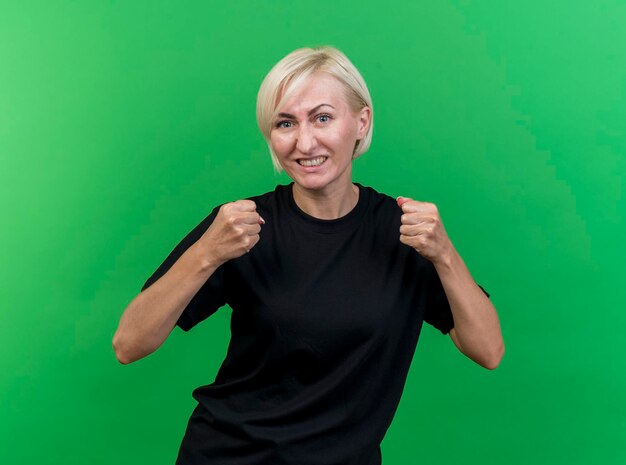 Joyful middle-aged blonde slavic woman looking at front doing yes gesture isolated on green wall