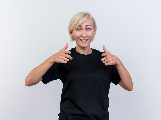 Joyful middle-aged blonde woman looking at front showing thumbs up isolated on white wall