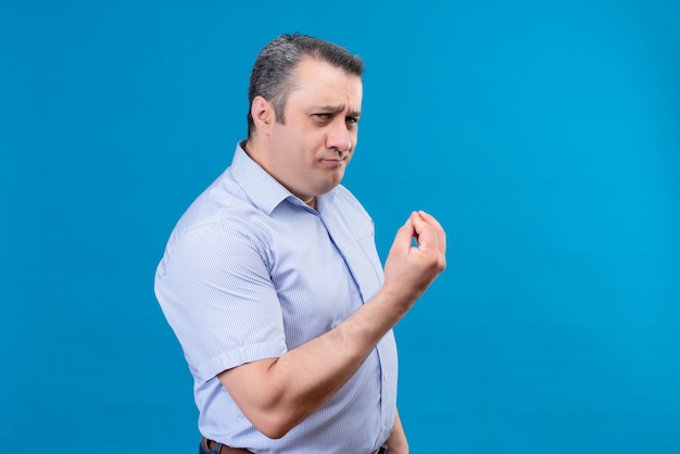 Радостный мужчина средних лет в синей рубашке в вертикальную полоску показывает вкусный жест рукой на синем фоне