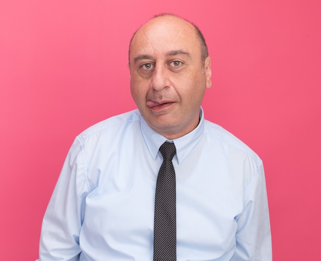 Joyful middle-aged man wearing white t-shirt with tie showing tongue isolated on pink wall