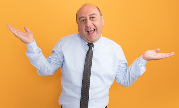Joyful middle-aged man wearing white t-shirt with tie spreading hands isolated on orange wall