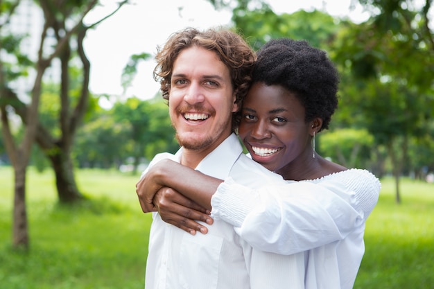 Joyful mix-raced couple cuddling in summer park