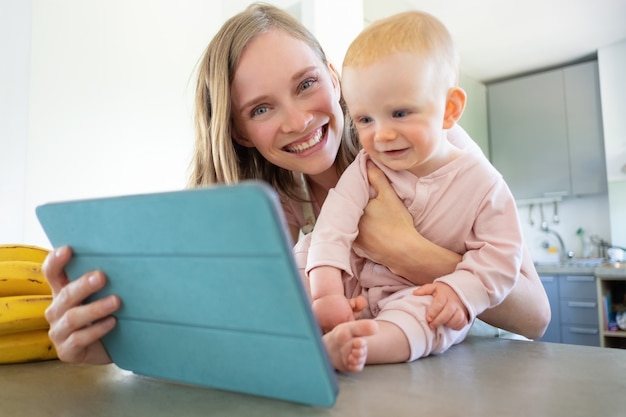 うれしそうなママと赤ちゃんが家族と話し、タブレットをビデオ通話に使用し、画面で一緒に笑っています。育児やオンラインコミュニケーションの概念