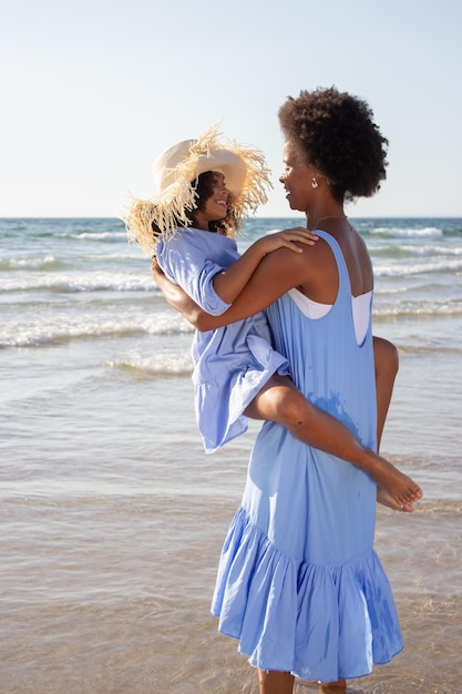 즐거운 엄마와 딸이 해변에서 놀고 있습니다. 아프리카계 미국인 가족은 걷고, 껴안고, 웃고, 장난을 치고 있습니다. 여가, 가족 시간, 유대감 개념