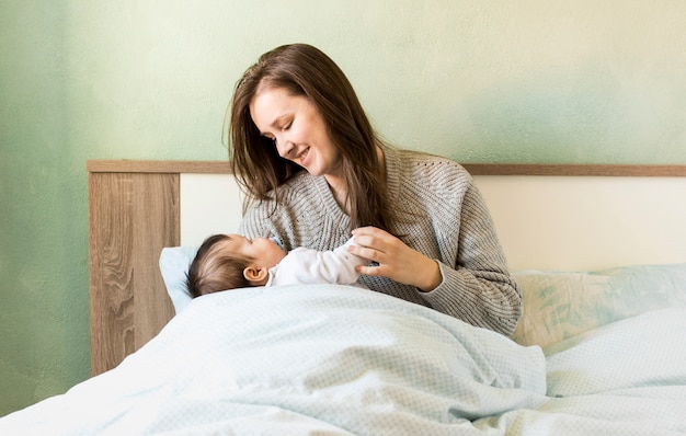 Joyful mother holding baby in arms in bed