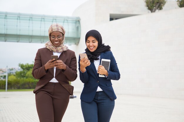 Joyful office female friends with smartphones chatting outside