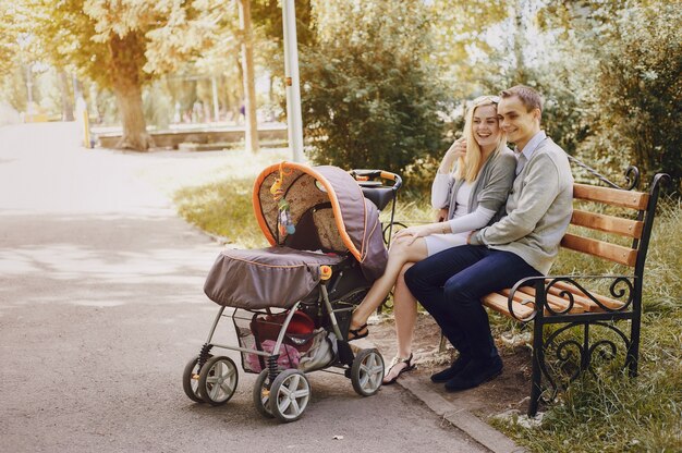 Радостные родители с коляской на скамейке в парке