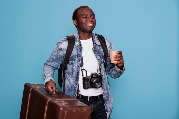 Радостный любитель фотографии с фотоаппаратом и багажом отправляется в путешествие на выходные. Счастливый фотограф с багажом и камерой DSLR готовится к путешествию в отпуск. Студийный снимок