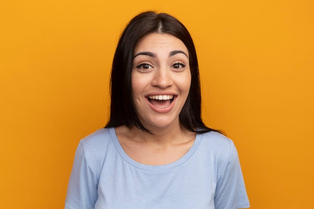 Joyful pretty brunette caucasian girl looks at camera on orange