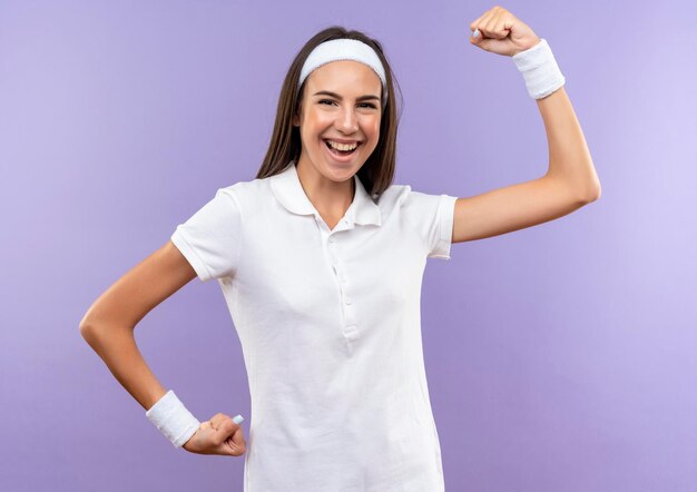 Радостная симпатичная спортивная девушка с ободком и браслетом жестко жестикулирует на фиолетовой стене