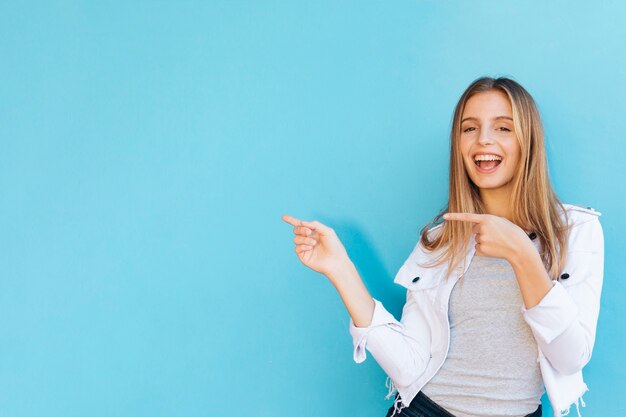 Joyful pretty young woman pointing her fingers against blue background