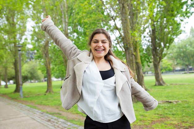 Joyful pretty young woman spreading arms in park