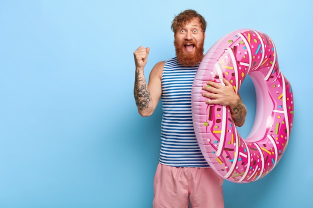 Free photo joyful red haired man posing with donut pool floaty