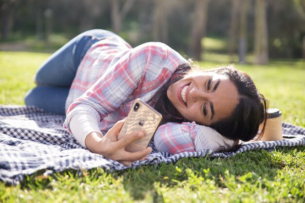Joyful relaxed student girl lying on plaid in park
