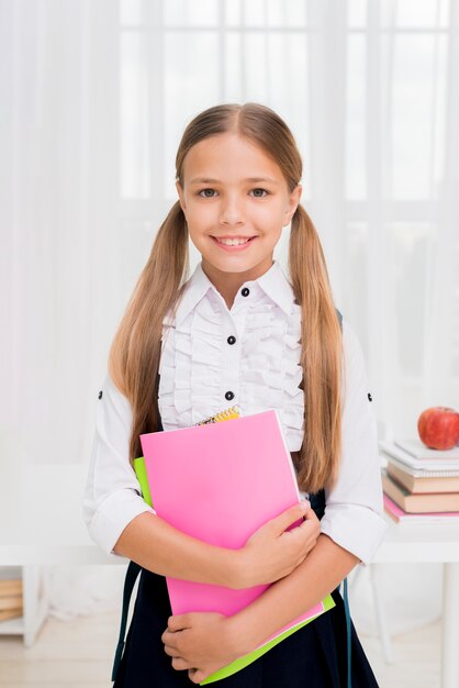 Joyful schoolgirl standing with bright workbooks