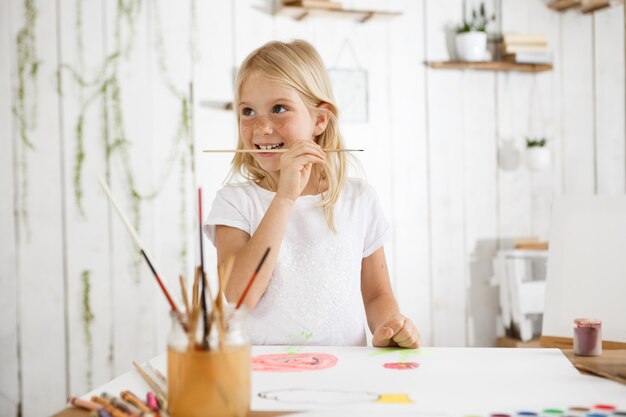 Joyful seven-year-old girl with blond hair and freckles looking happy in white clothes.