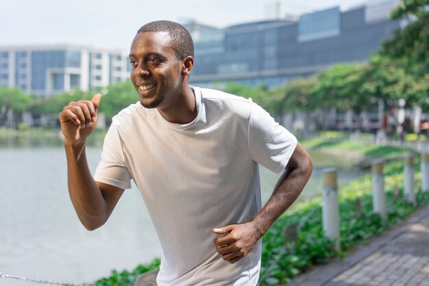 Joyful sporty black guy running by city pond.