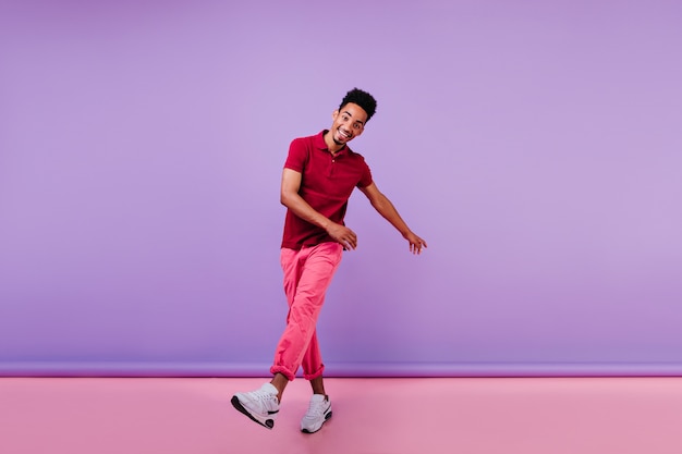 Joyful sporty guy in pink pants expressing happiness. emotional black young man dancing.