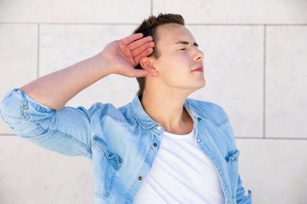 Joyful student guy with closed eyes making listening sign